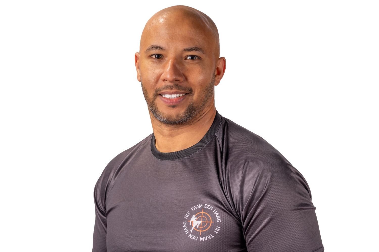 Athletic person wearing a gray t-shirt with a logo smiles while standing against a white background.