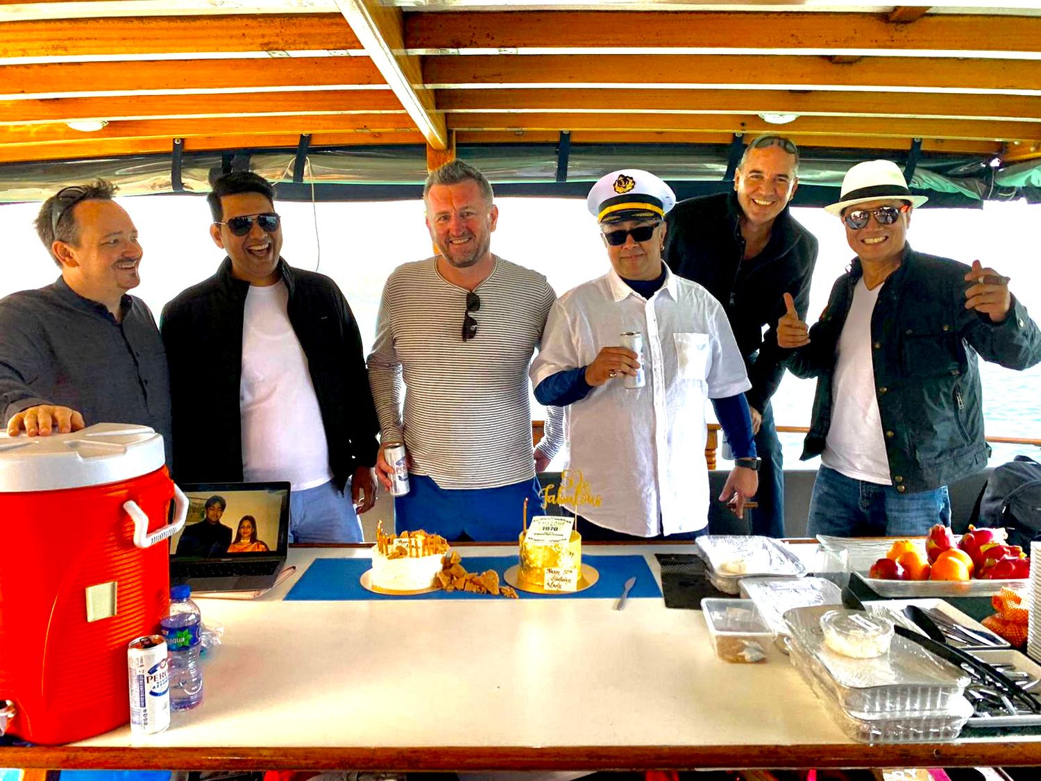 People gathered around a table with food and drinks on a boat deck.