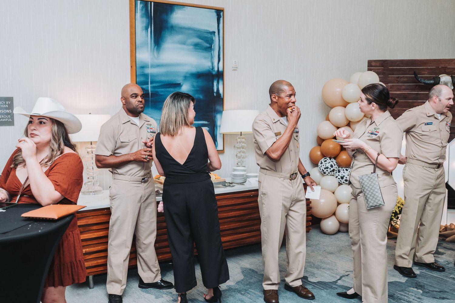 People in uniforms and formal wear socialize at an event with balloon decorations.