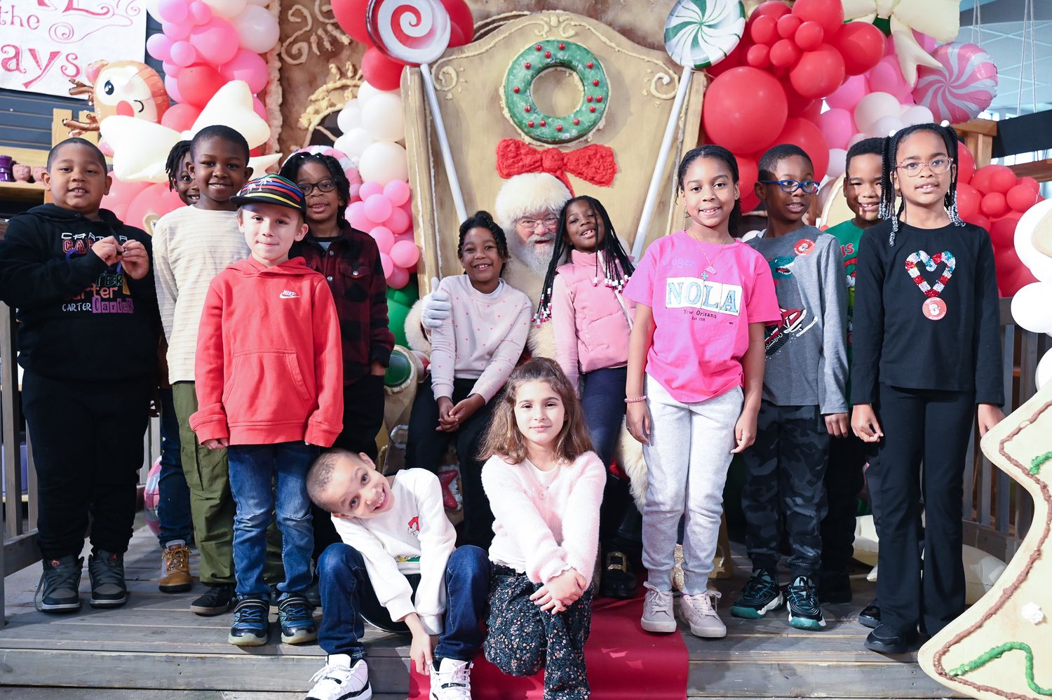 A large group poses together at a pink-themed charity or fundraising event with decorative balloons.
