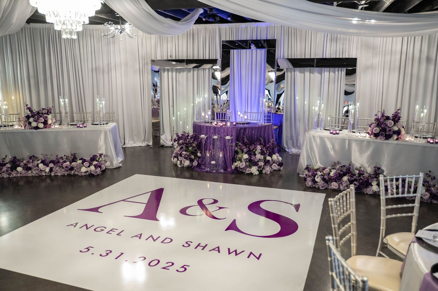 Elegant wedding reception venue with purple lighting, white draping, and personalized dance floor monogram.