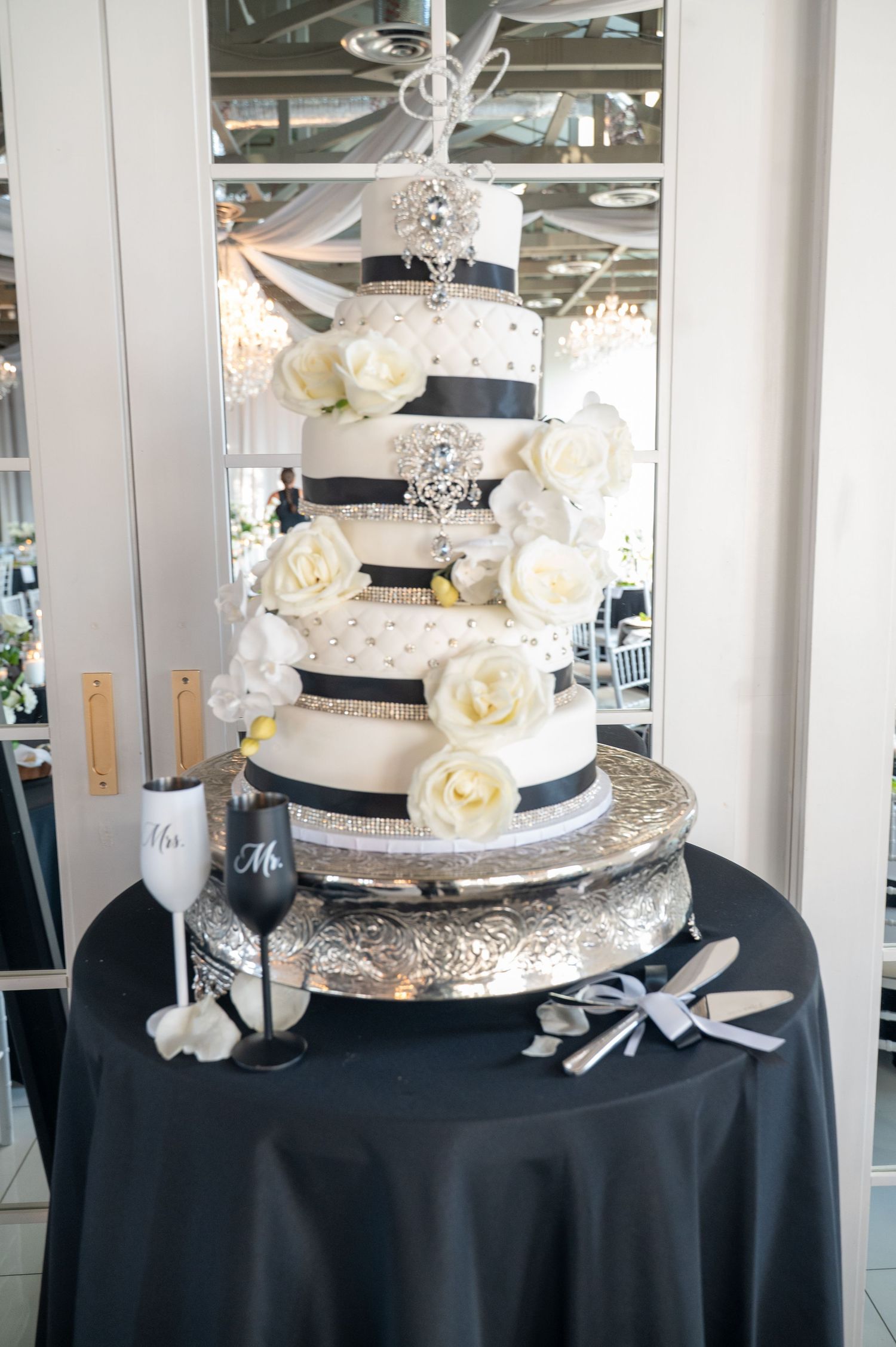 Elegant white wedding cake with silver accents and fresh flowers on black tablecloth.