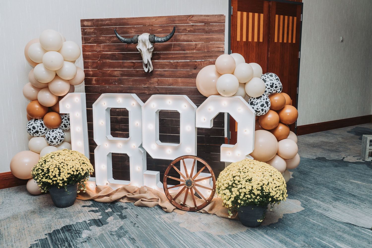 Rustic wedding decor featuring balloon arch, wooden backdrop and 'I DO' letters with floral accents.