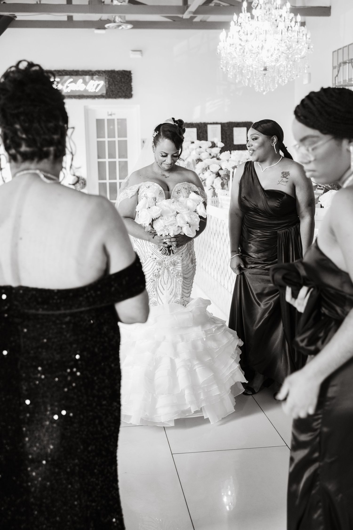 Wedding party in black dresses and white gown posing together in an elegant venue with chandeliers.