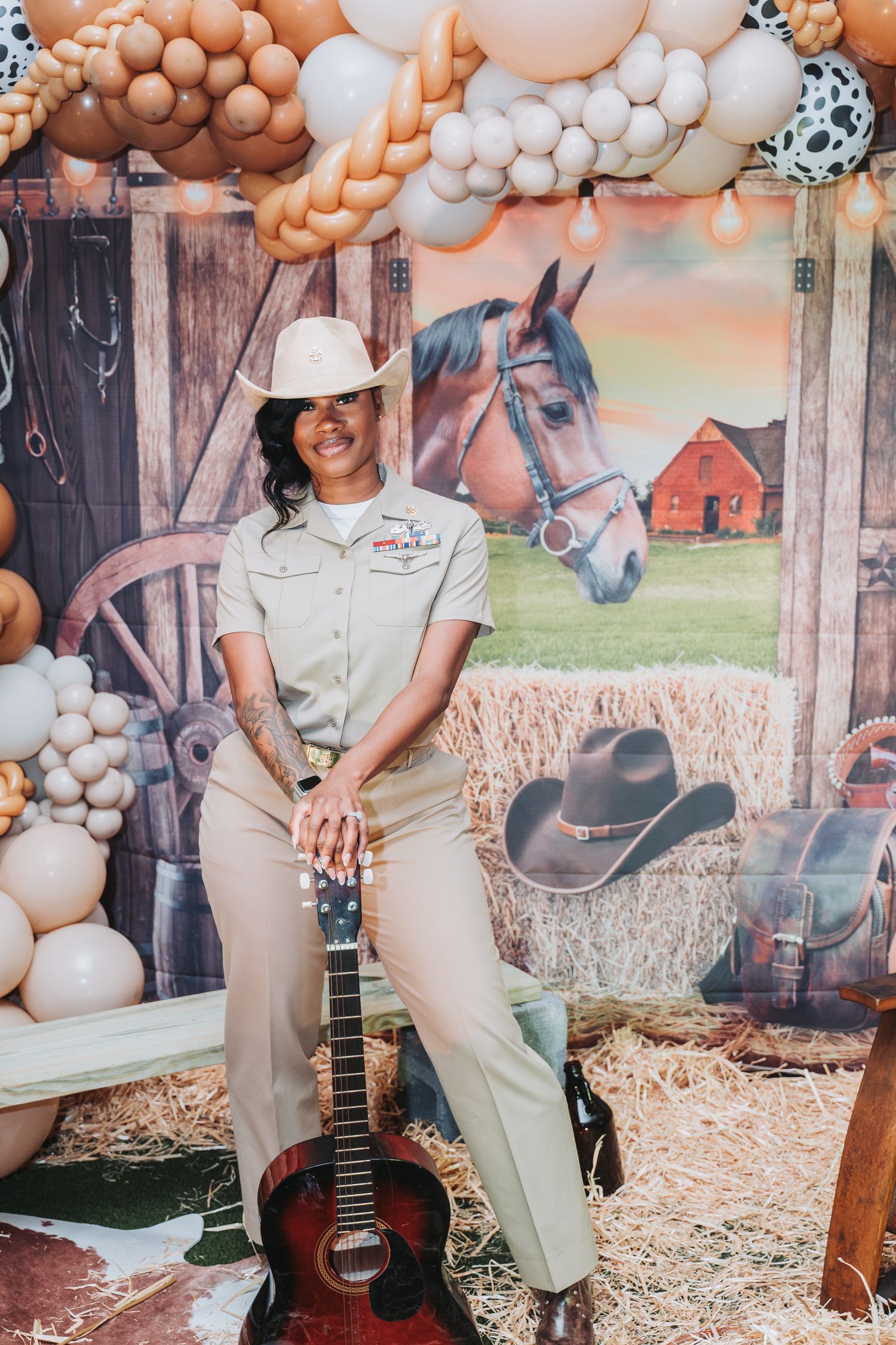 Navy Chief poses with guitar against western-themed backdrop with horse and balloon decorations.