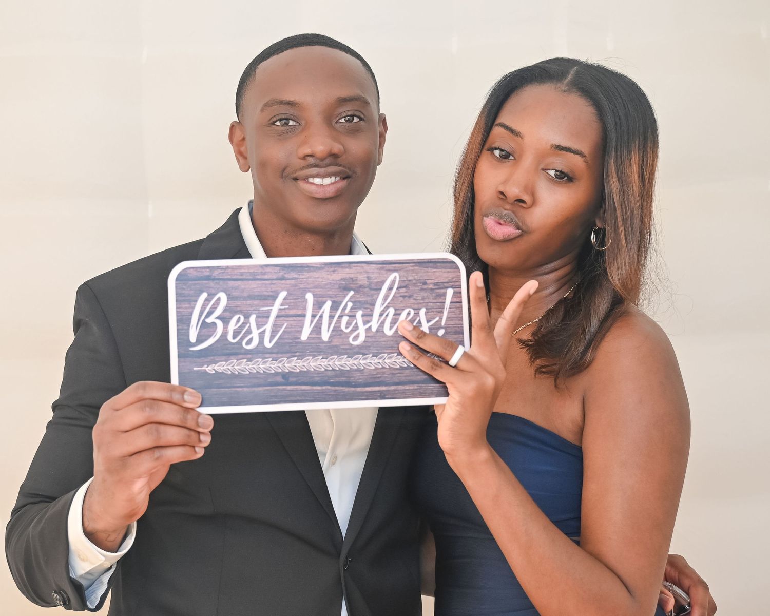Couple holding a 'Best Wishes' sign while posing for a celebratory photo.