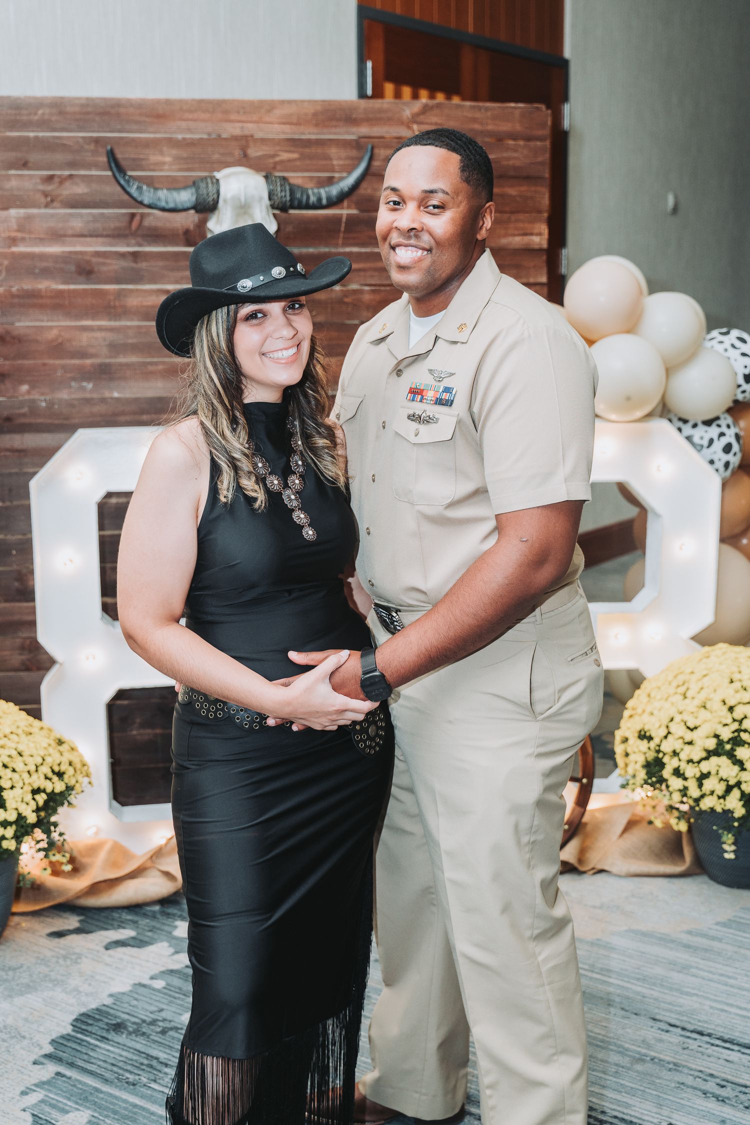 Couple posing in front of western-themed wedding decor with balloons and rustic elements.