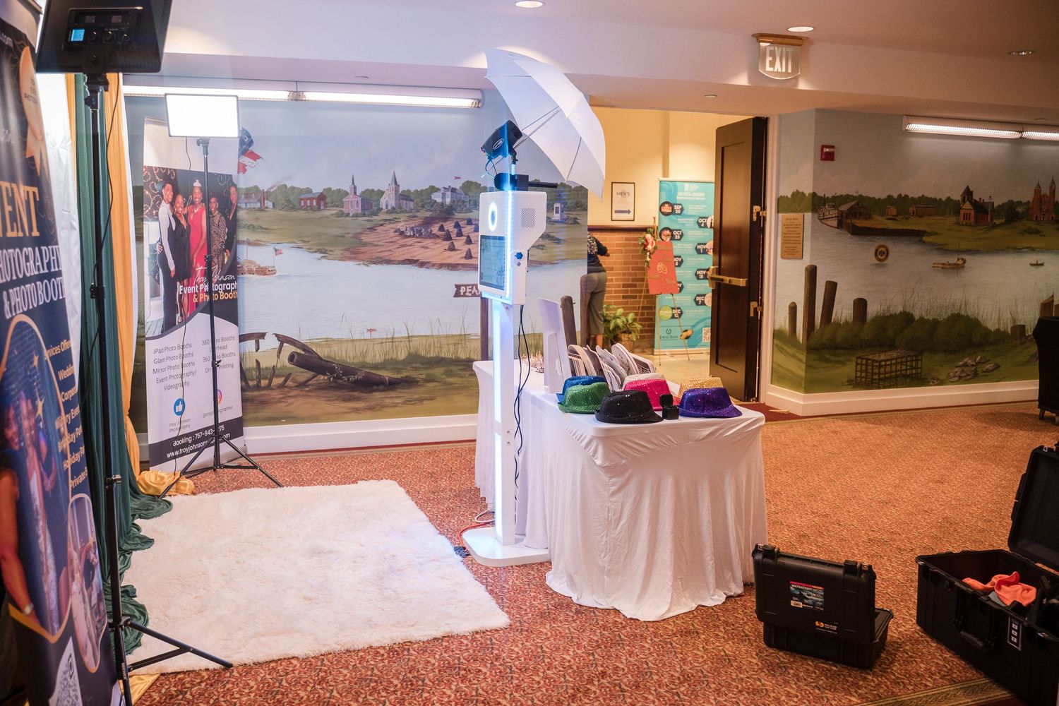 A decorated wedding arch and display table setup in a carpeted room with landscape murals on the walls.