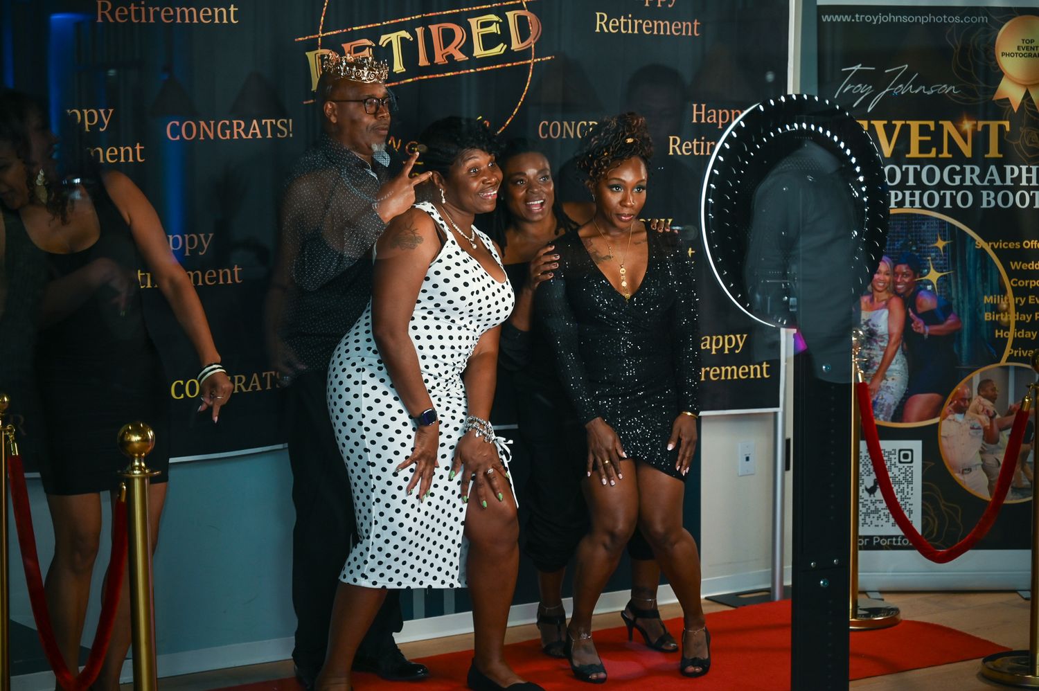 A group of people pose together on a red carpet at an event with promotional signage in the background.