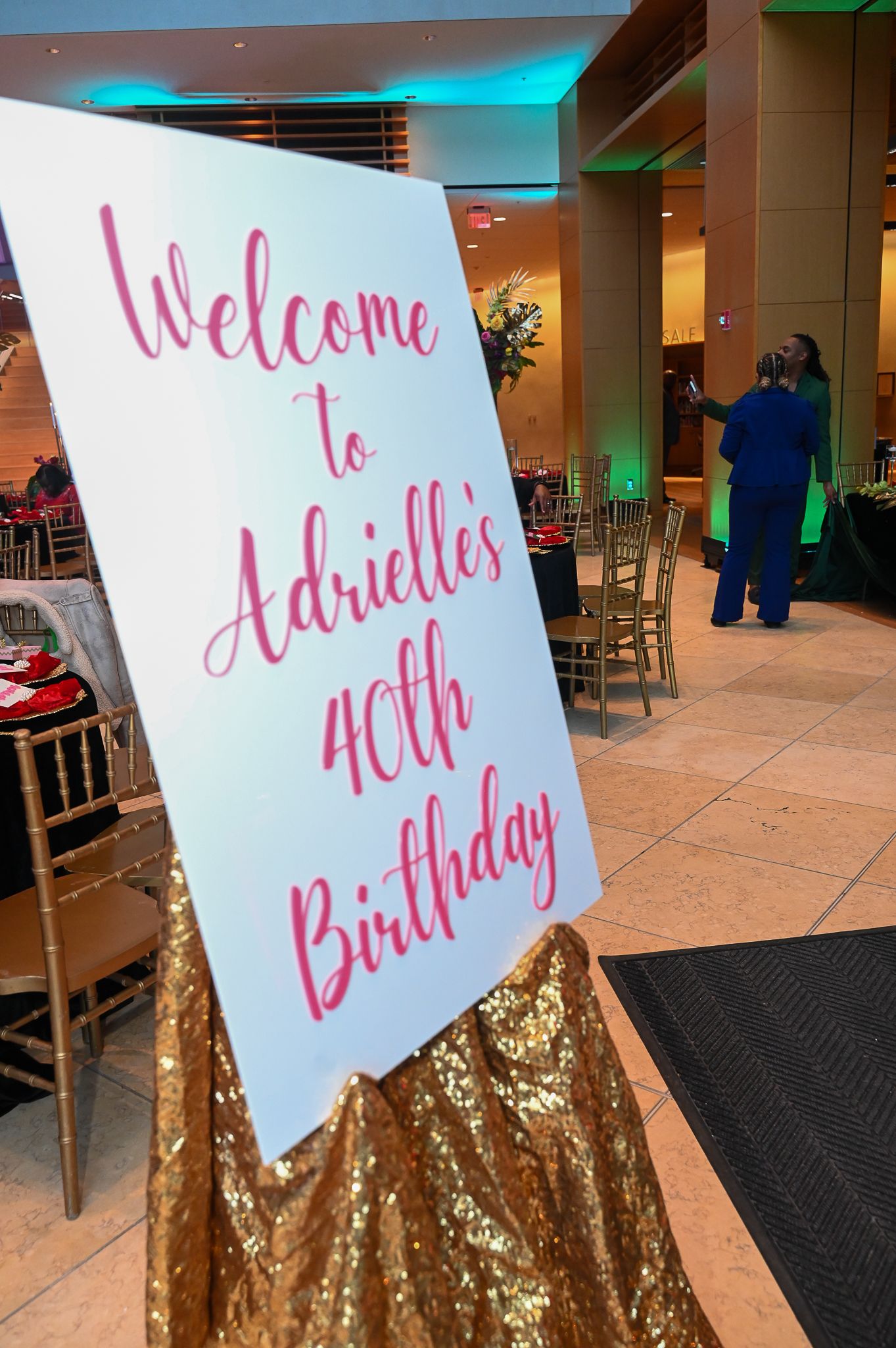 Birthday welcome signs with pink lettering displayed on gold sequin stands at an event entrance.