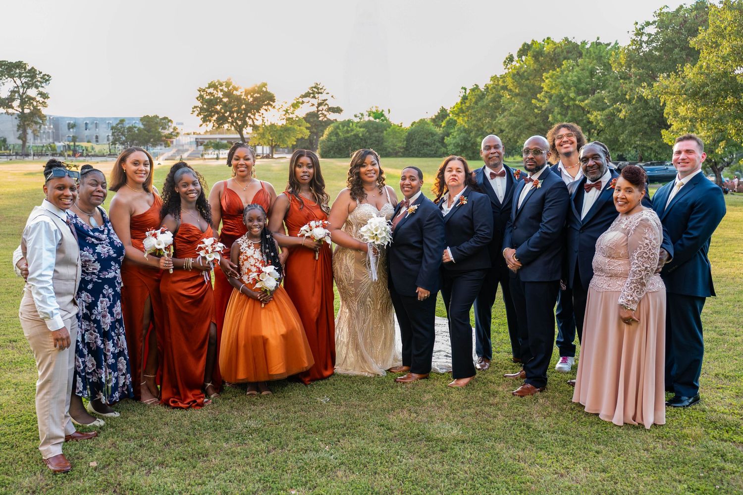 Wedding party members pose outdoors wearing autumn-toned dresses and formal suits.