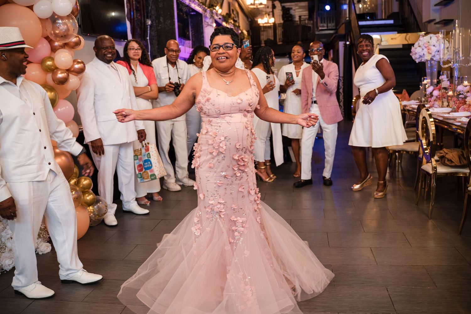 A person in a blush pink mermaid gown dances at an all-white dress code celebration.