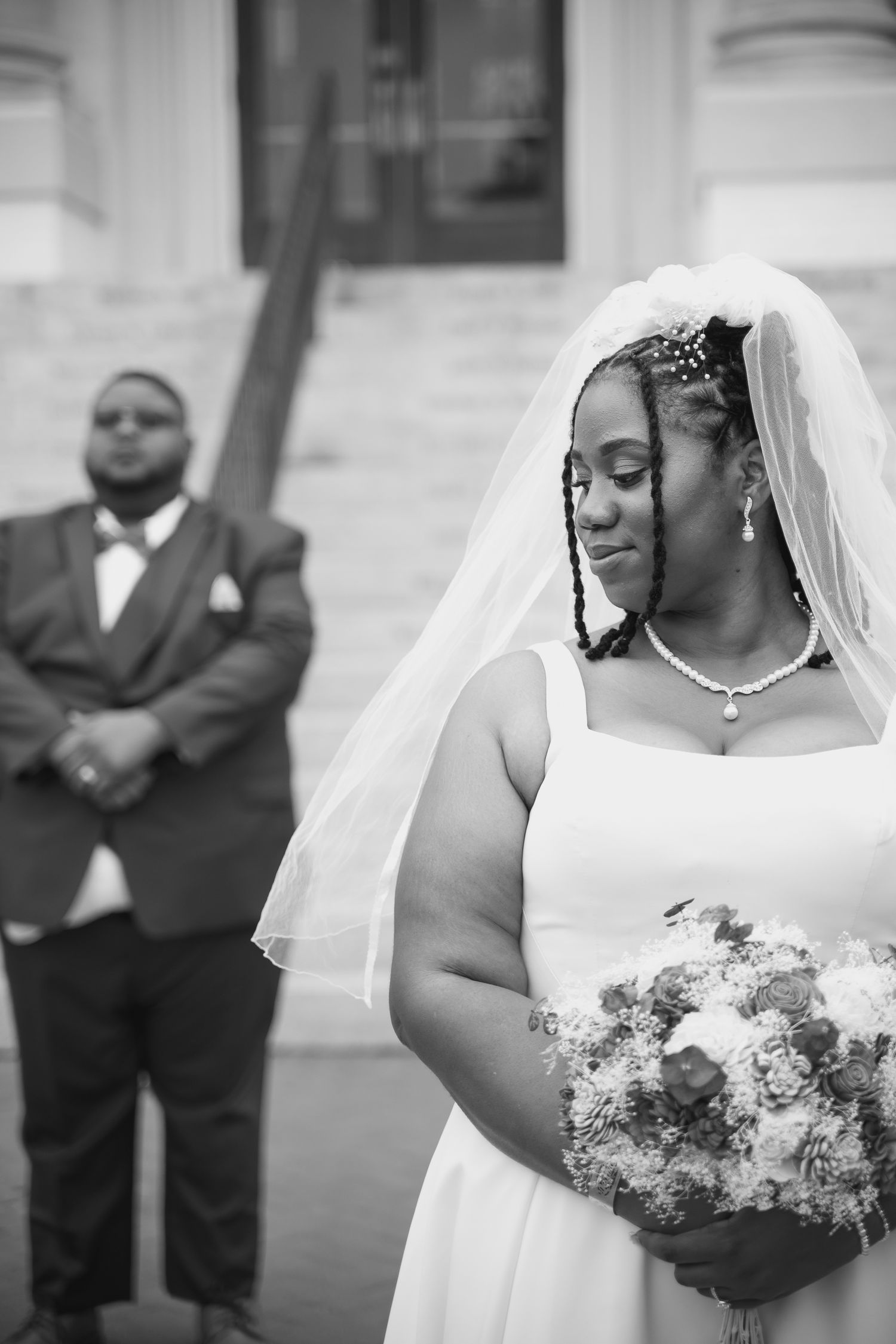 Elegant bride in white dress and veil poses with bouquet for wedding portraits.