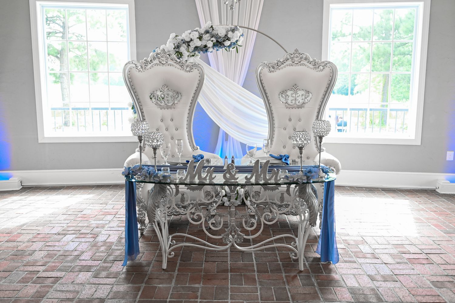 Ornate white throne chairs with blue accent and floral decorations set up for wedding ceremony.