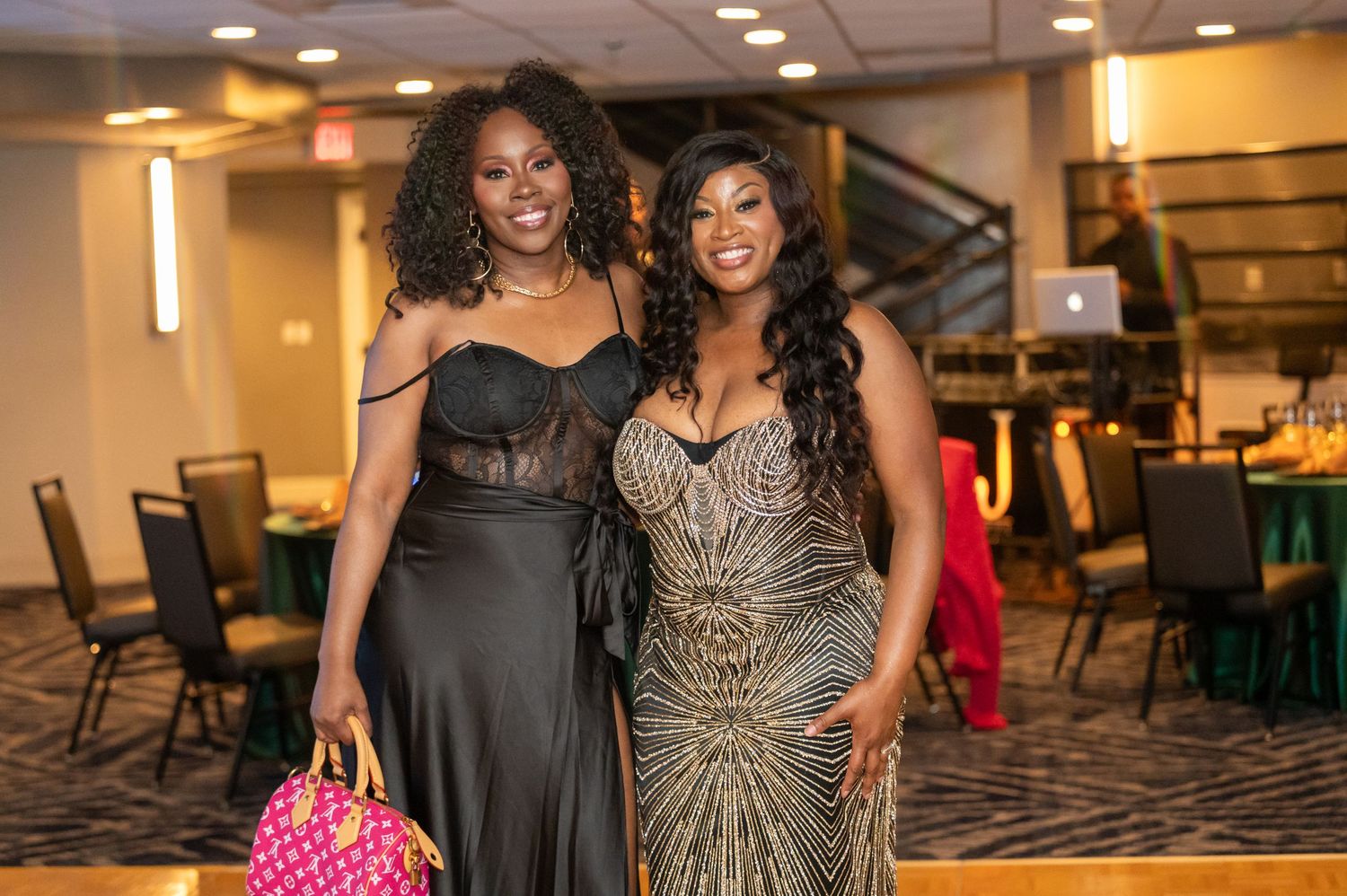 Formal event attendees in elegant black and sparkly dresses pose together at an indoor venue.