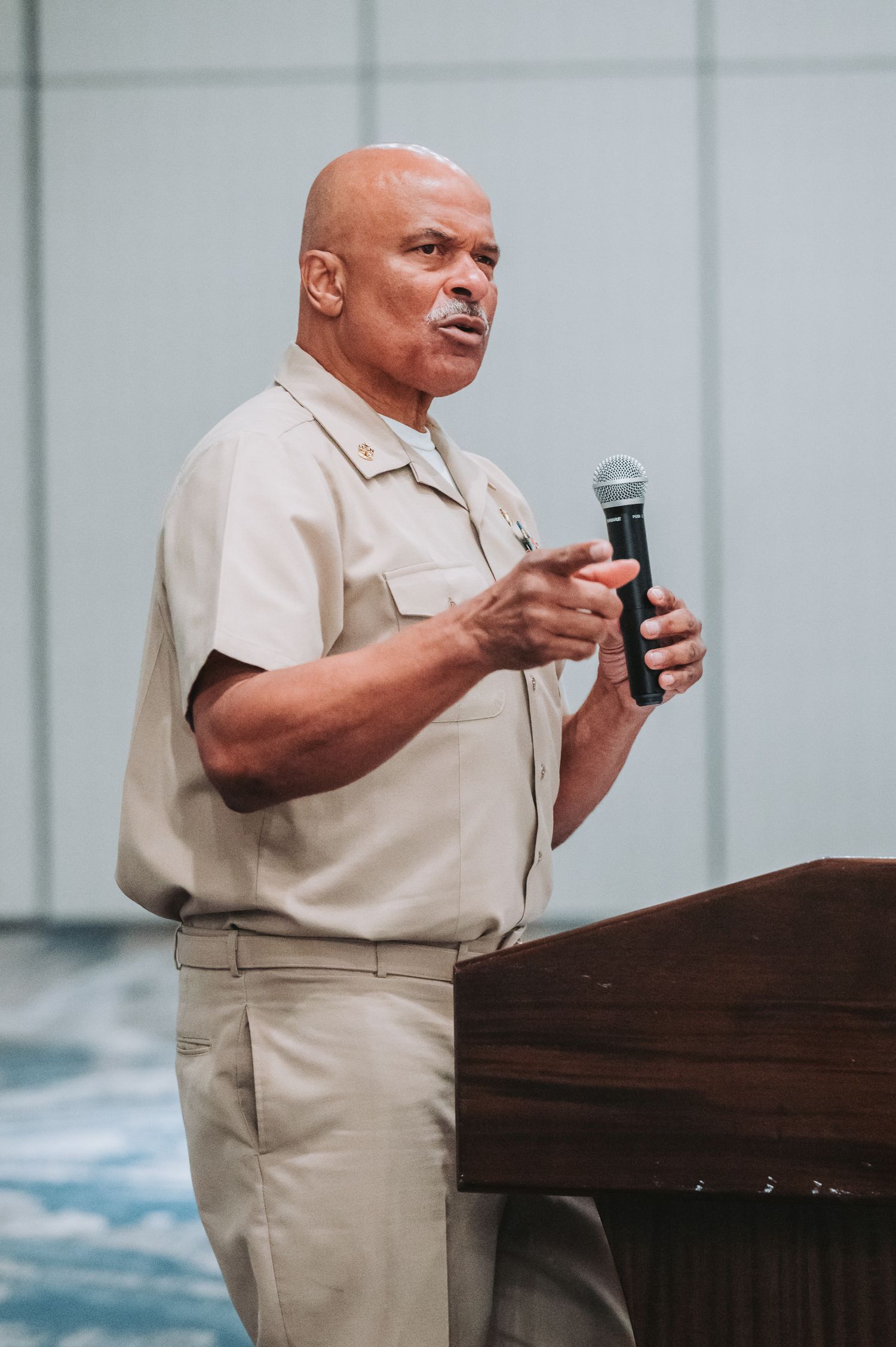 Speaker in tan uniform delivering presentation at wooden podium.