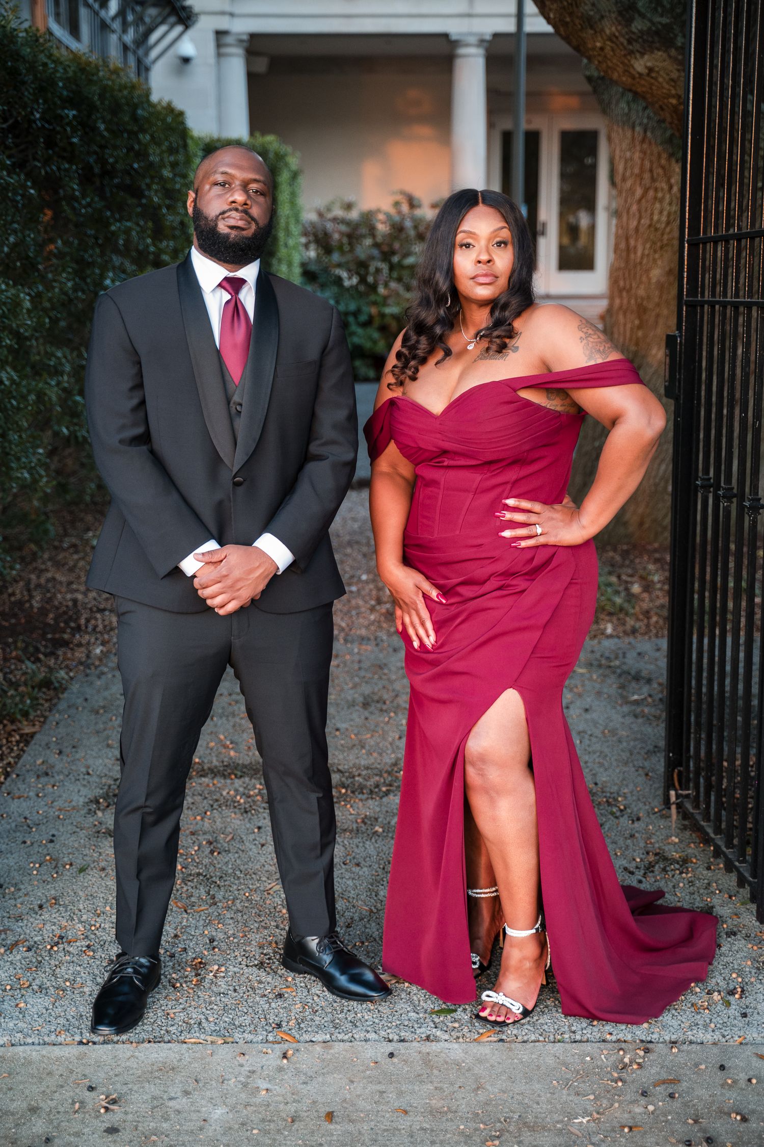A couple in formal wear strikes playful poses in a series of outdoor photos against a brick wall.