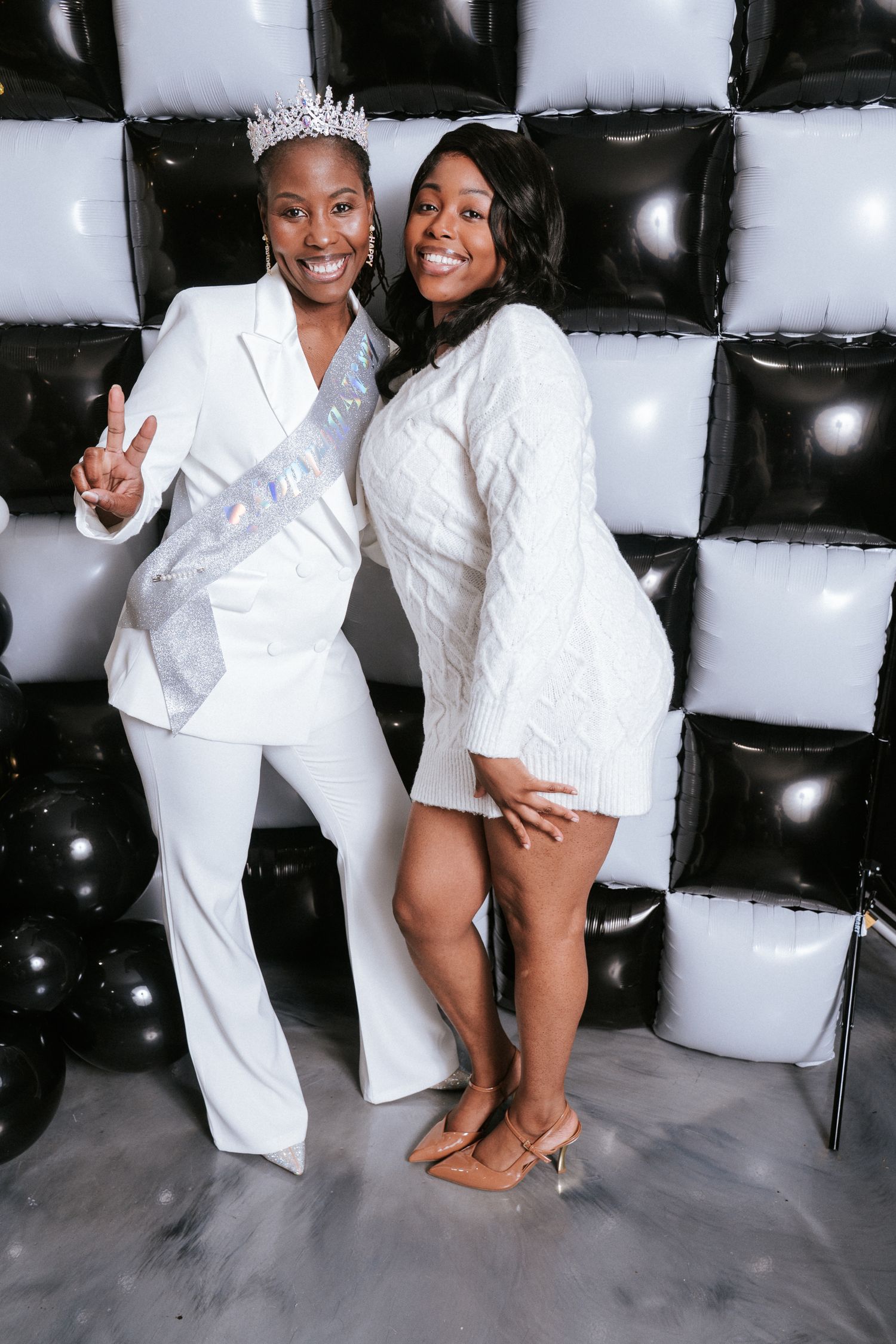 Two people wearing white outfits pose playfully together in a studio setting with white blocks in the background.
