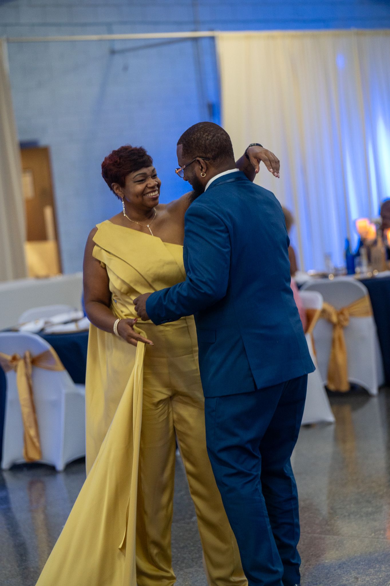 Elegant dance scene with guests in formal attire including yellow gown and navy suit.