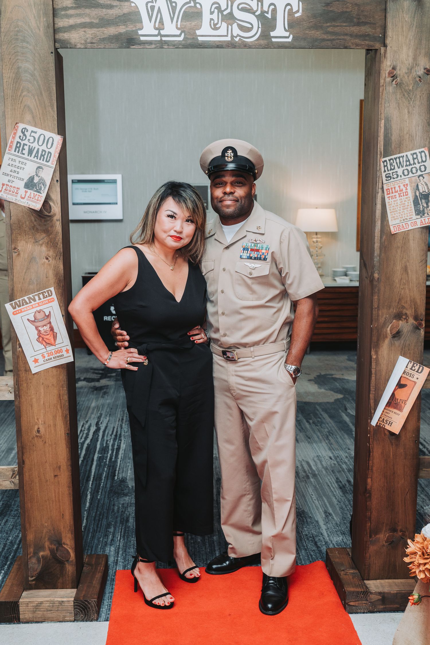 A couple poses in front of a western-themed backdrop with vintage wanted posters.