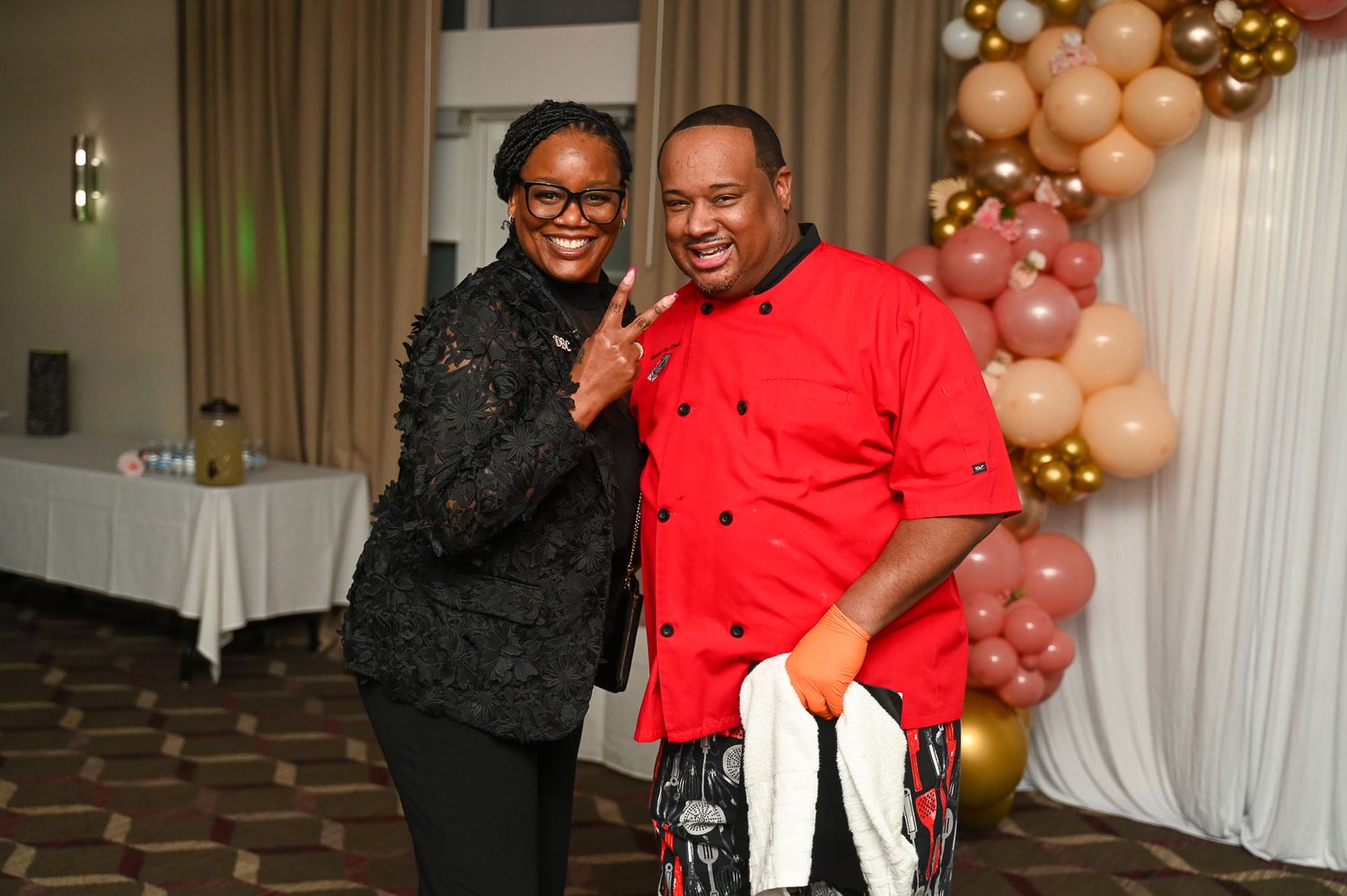 Party guests celebrate at an event with pink and gold balloon decorations in the background.