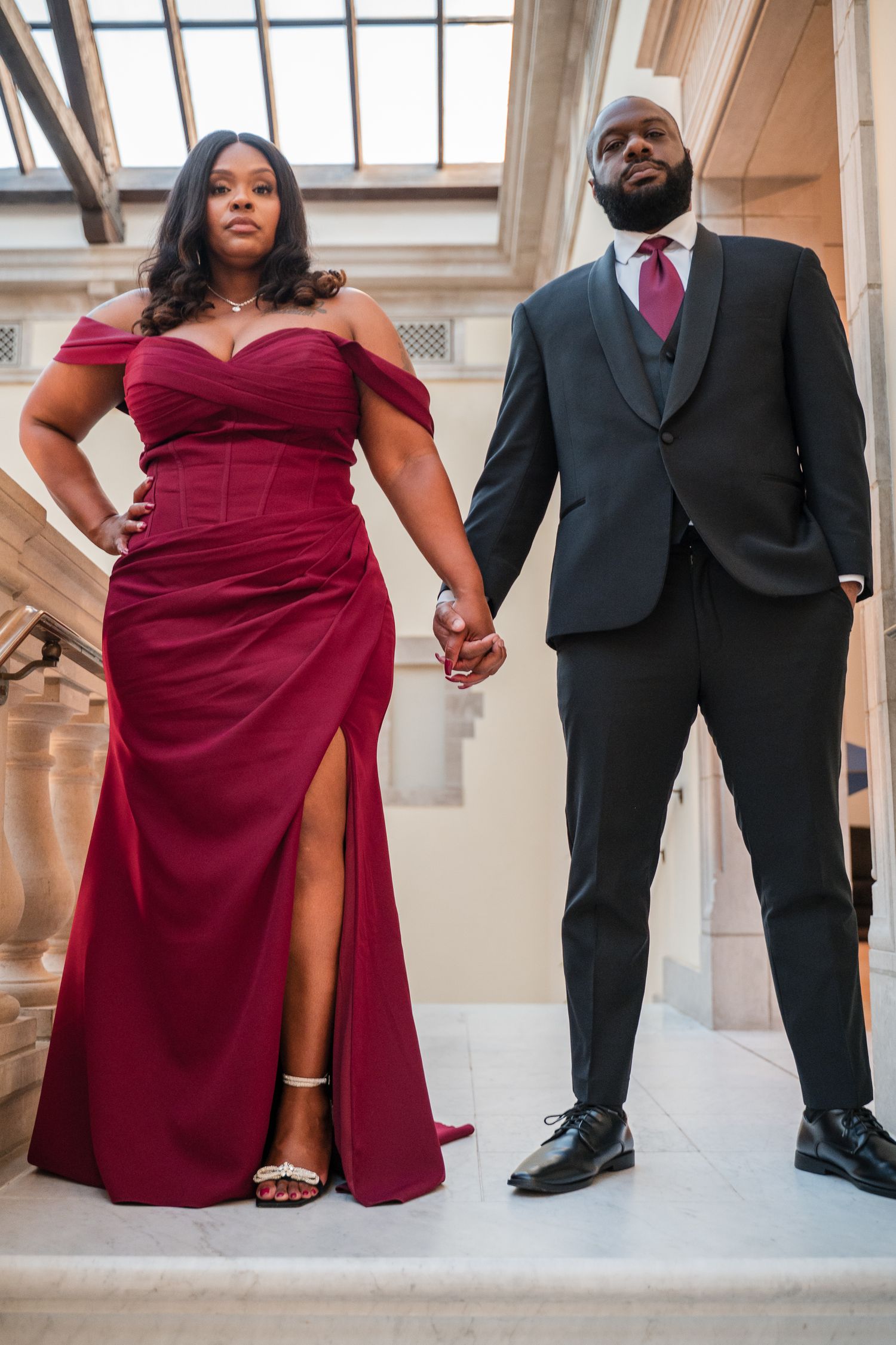 A stylish couple poses on white marble steps, showcasing formal attire and elegant poses.