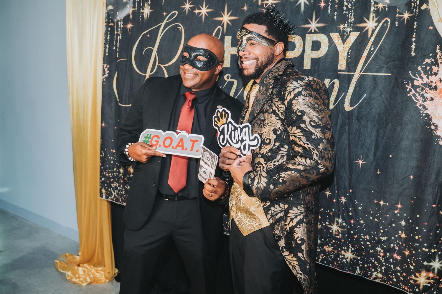 Two people pose with props in front of a sparkly backdrop at a photo booth.