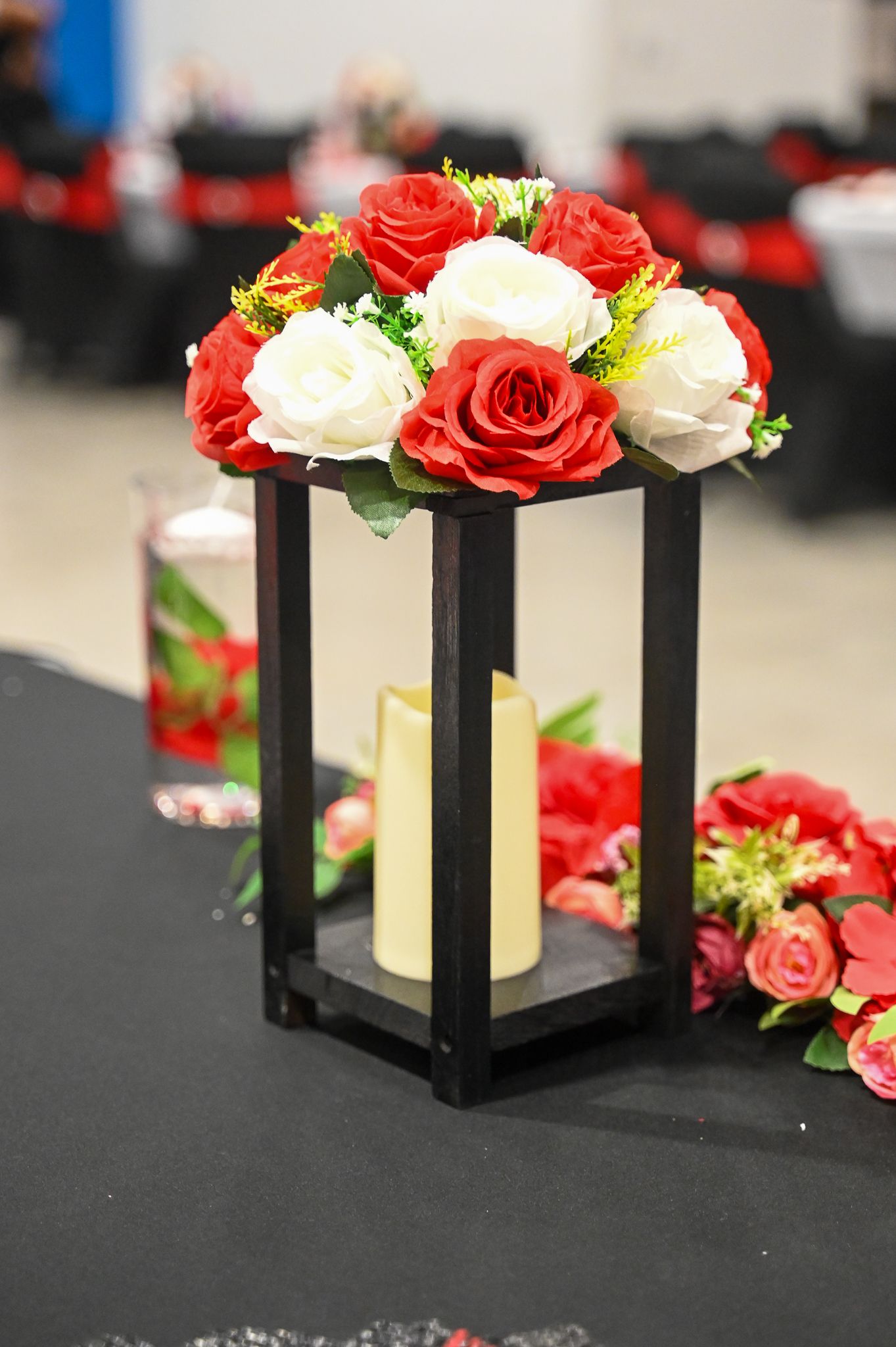 Black lantern centerpiece decorated with red and white roses on a dark table.