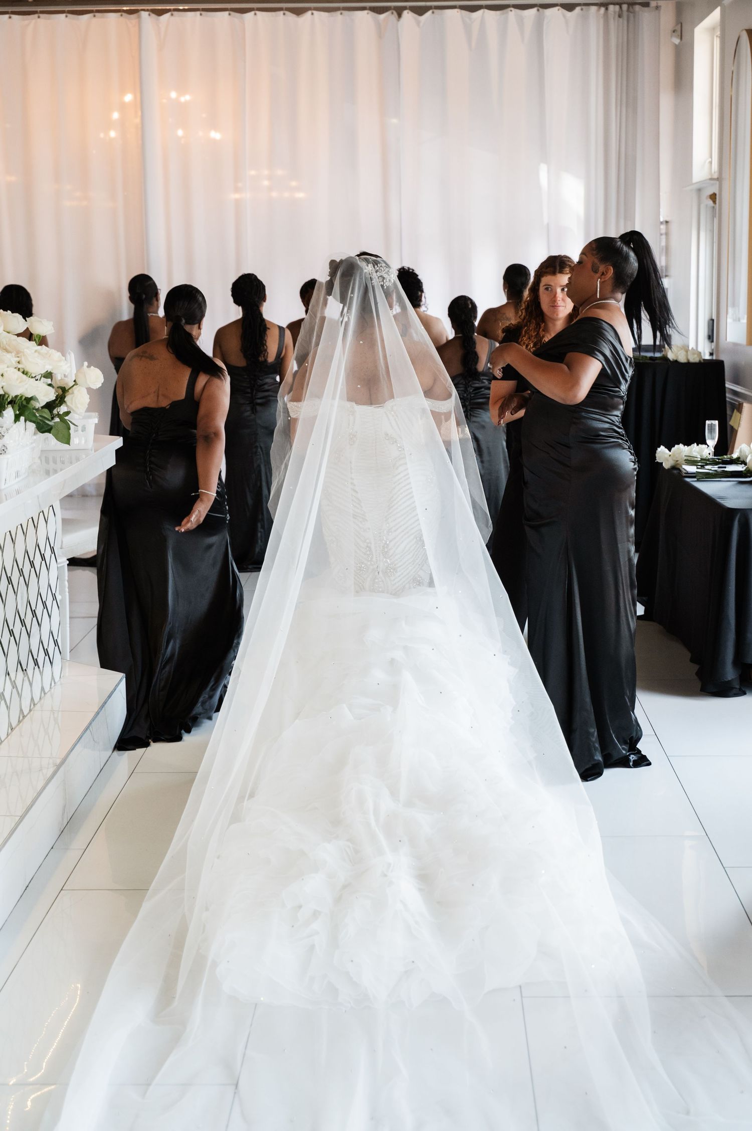 Wedding party in black dresses gathered around a bride in a flowing white gown.