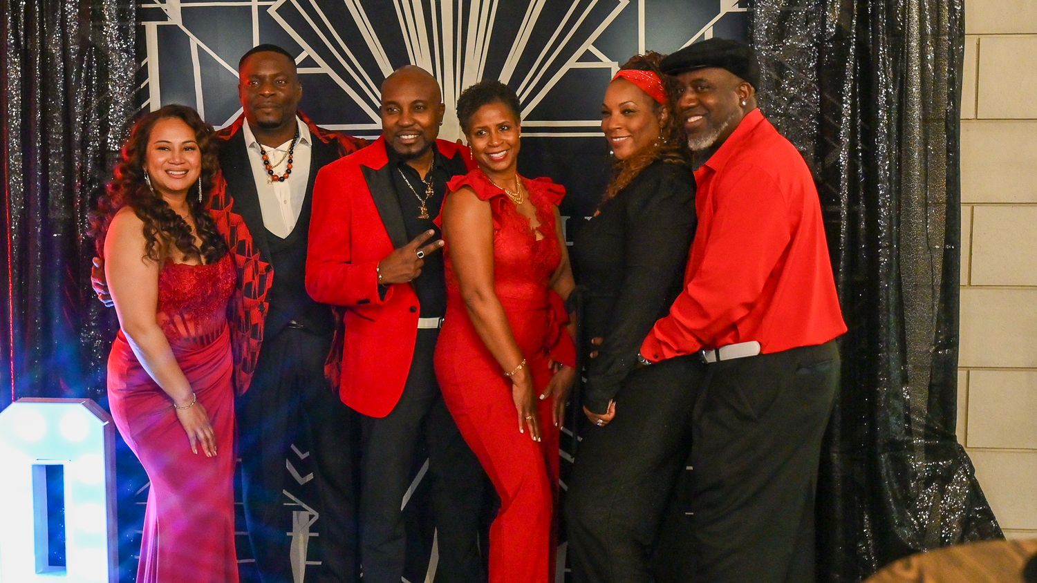 A group of party guests pose together in formal attire at an elegant event with sparkly decorations.