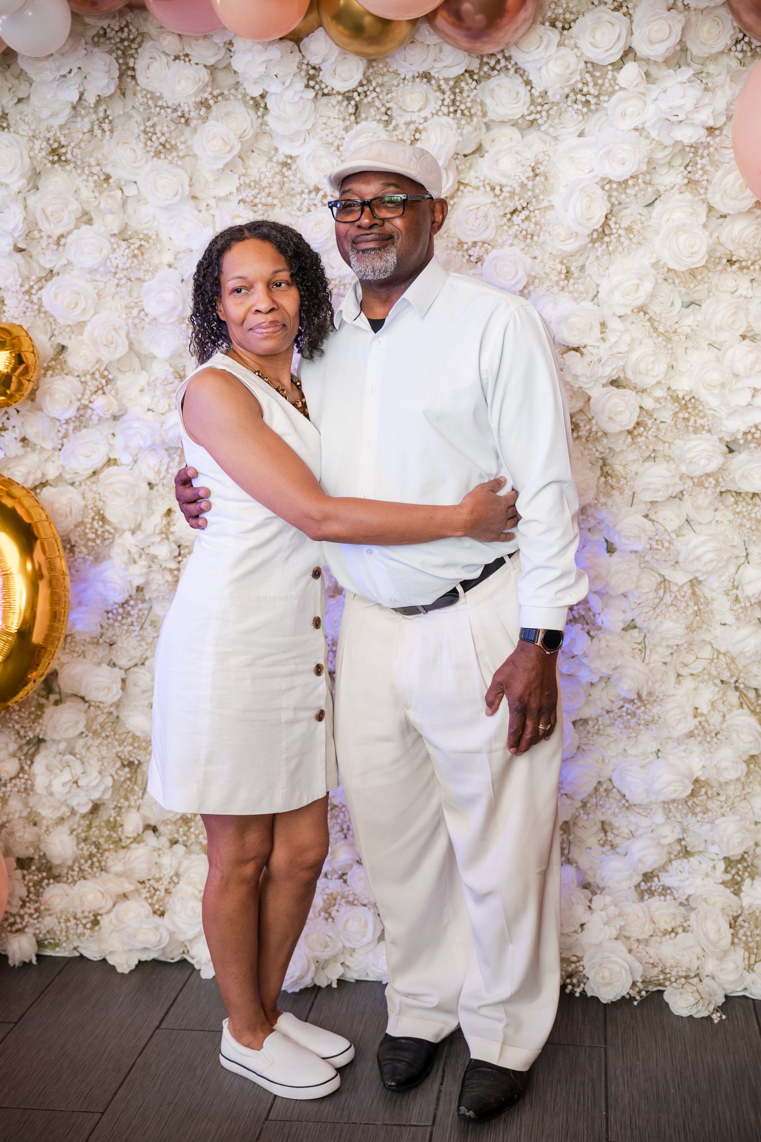 Elegant all-white party setup with floral backdrop and balloon decorations.