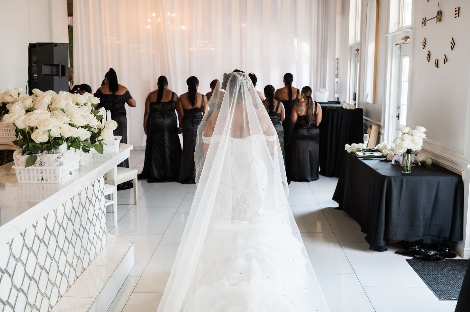 Wedding ceremony setup with bridesmaids in black dresses standing behind long white veil trailing on floor.