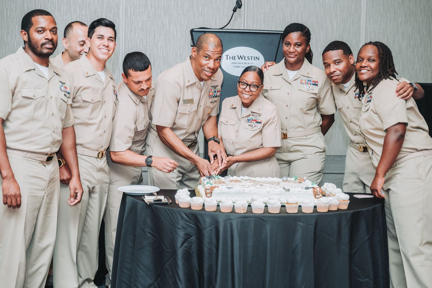 People in matching uniforms gather around a table with cupcakes at a celebration.