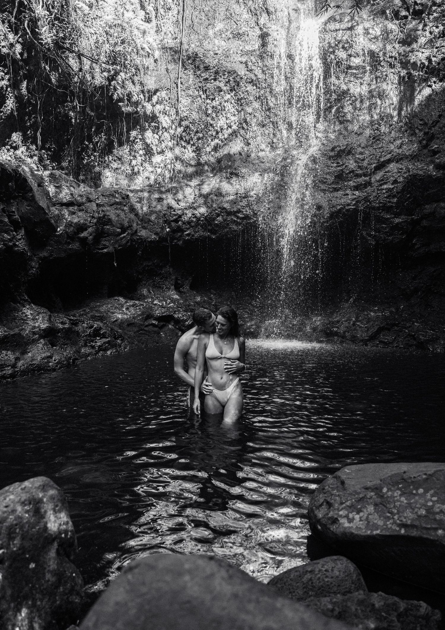 A black and white photo series shows swimmers enjoying a natural cenote pool beneath a waterfall in Mexico.