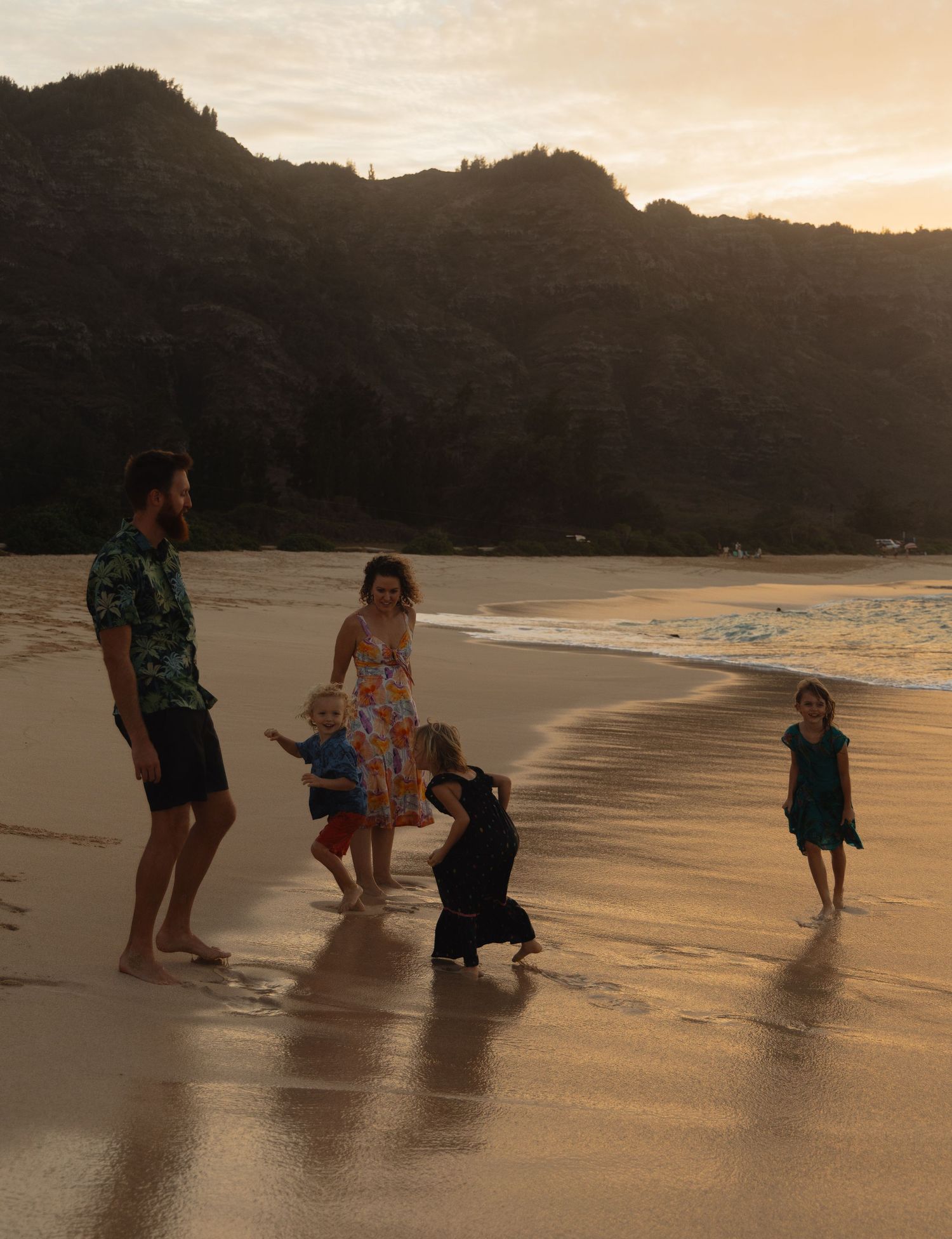 A group plays in the shallow ocean water at sunset, creating silhouettes against the golden sky and beach.