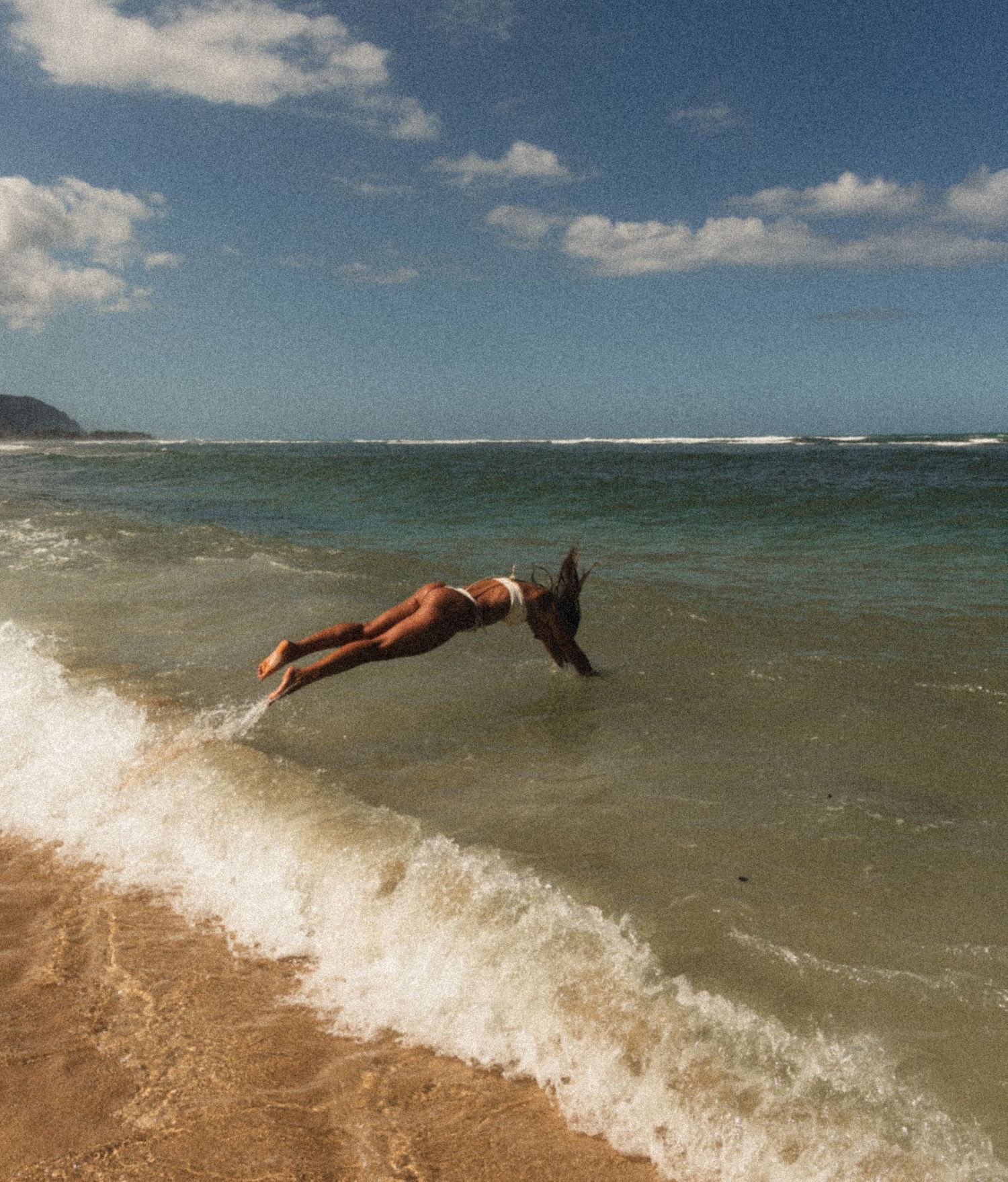 A sequence showing someone diving into an incoming ocean wave at the beach.