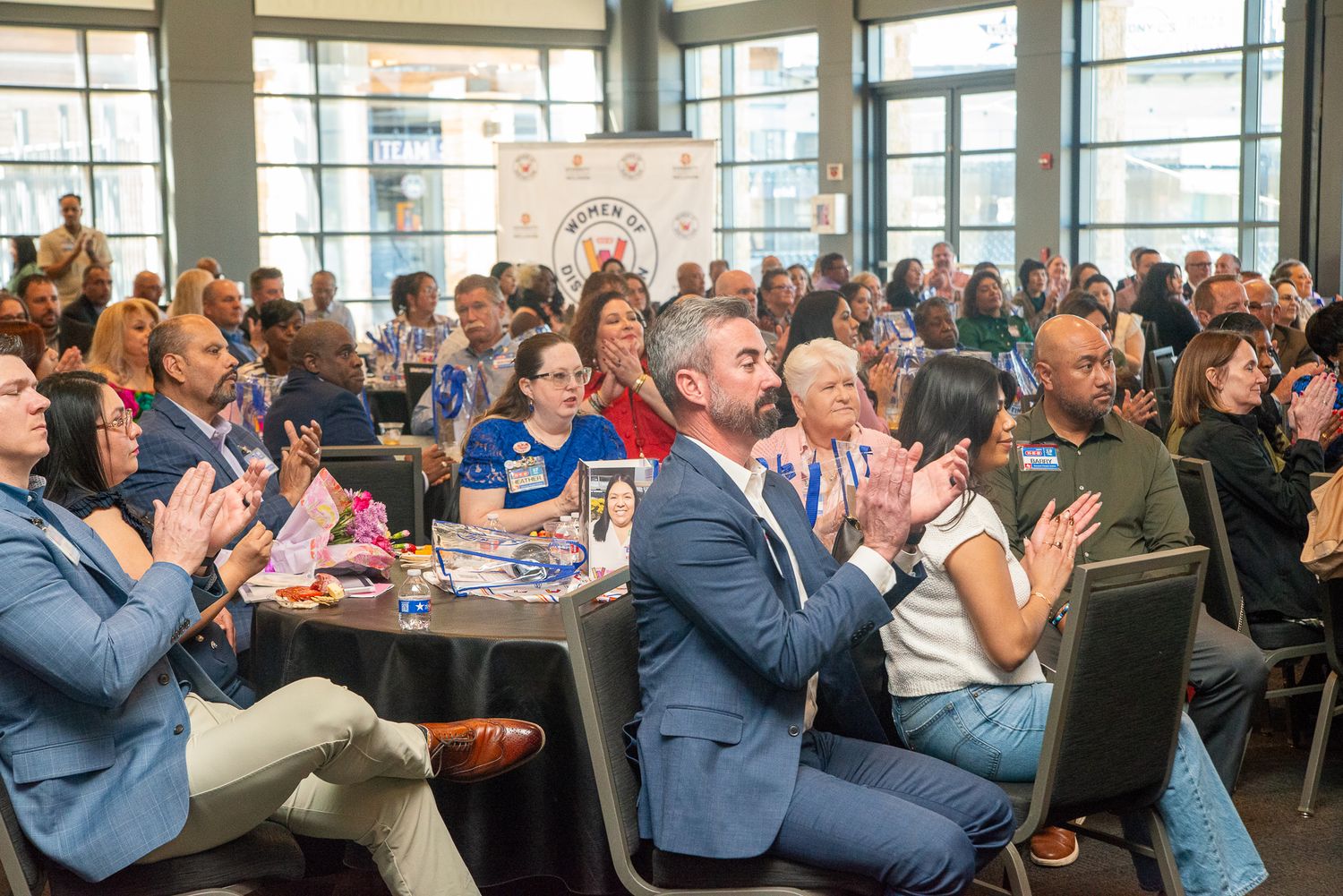 Large crowd of attendees clapping during a professional business conference in modern venue.