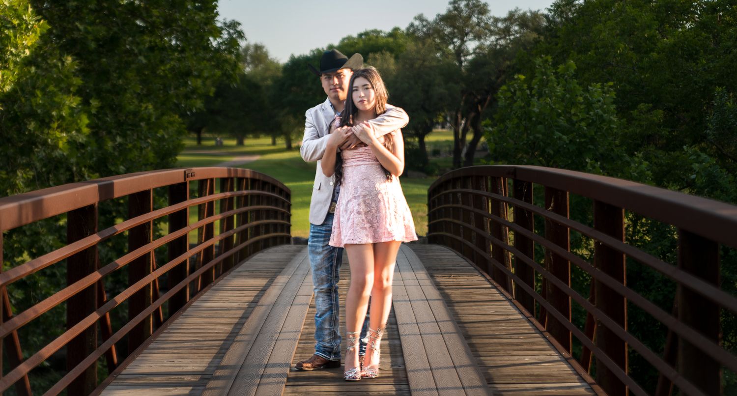 A rustic wooden bridge walkway extends through lush green trees in a park setting.
