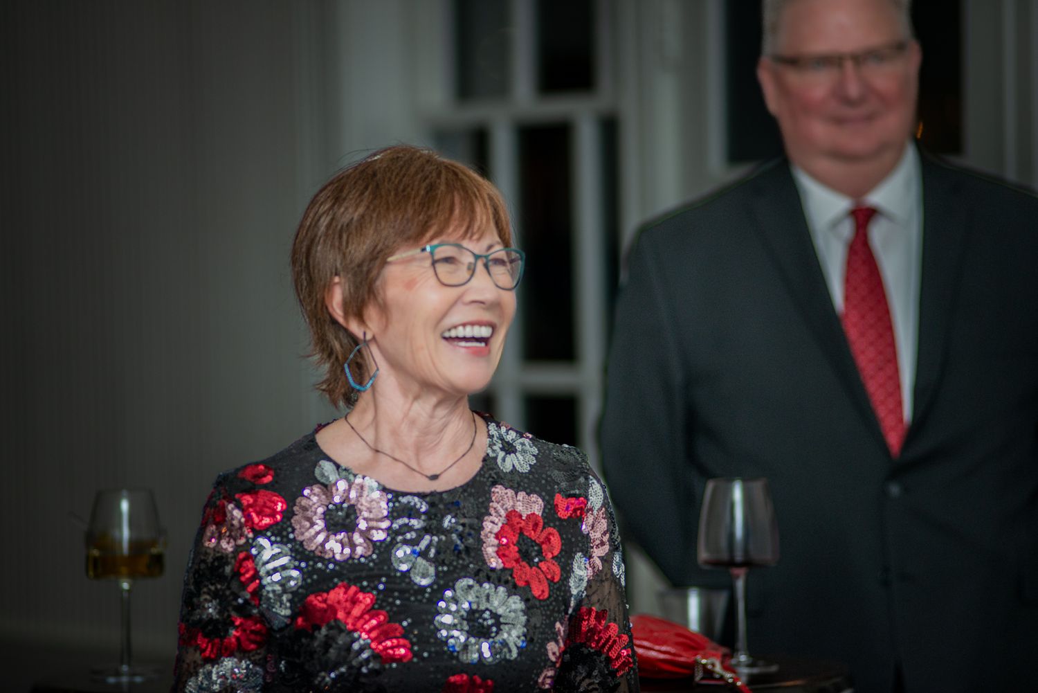 A woman in a floral dress laughs joyfully at a social gathering.