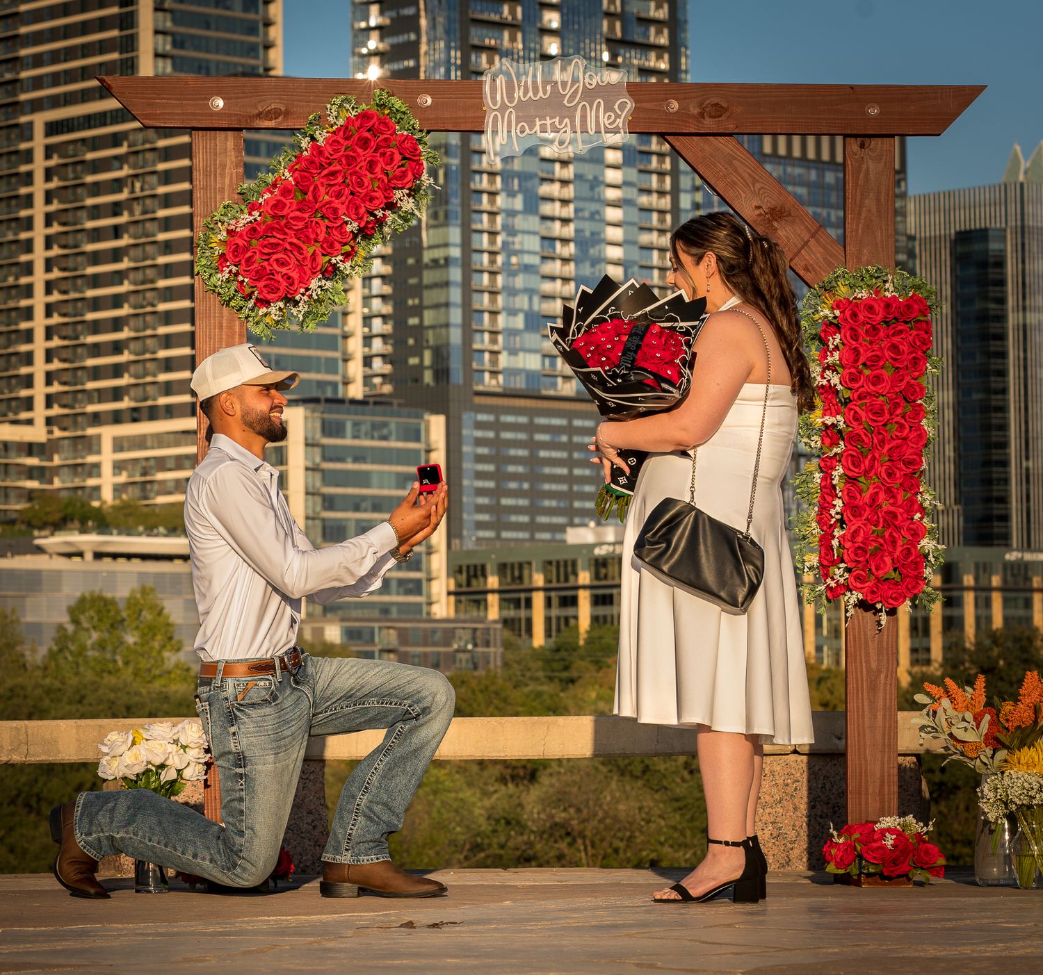 A panoramic proposal scene with bright red flowers and city buildings in the background.