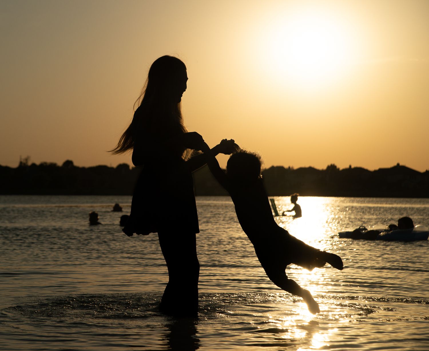 Silhouette of person and dog playing in water against golden sunset over lake.