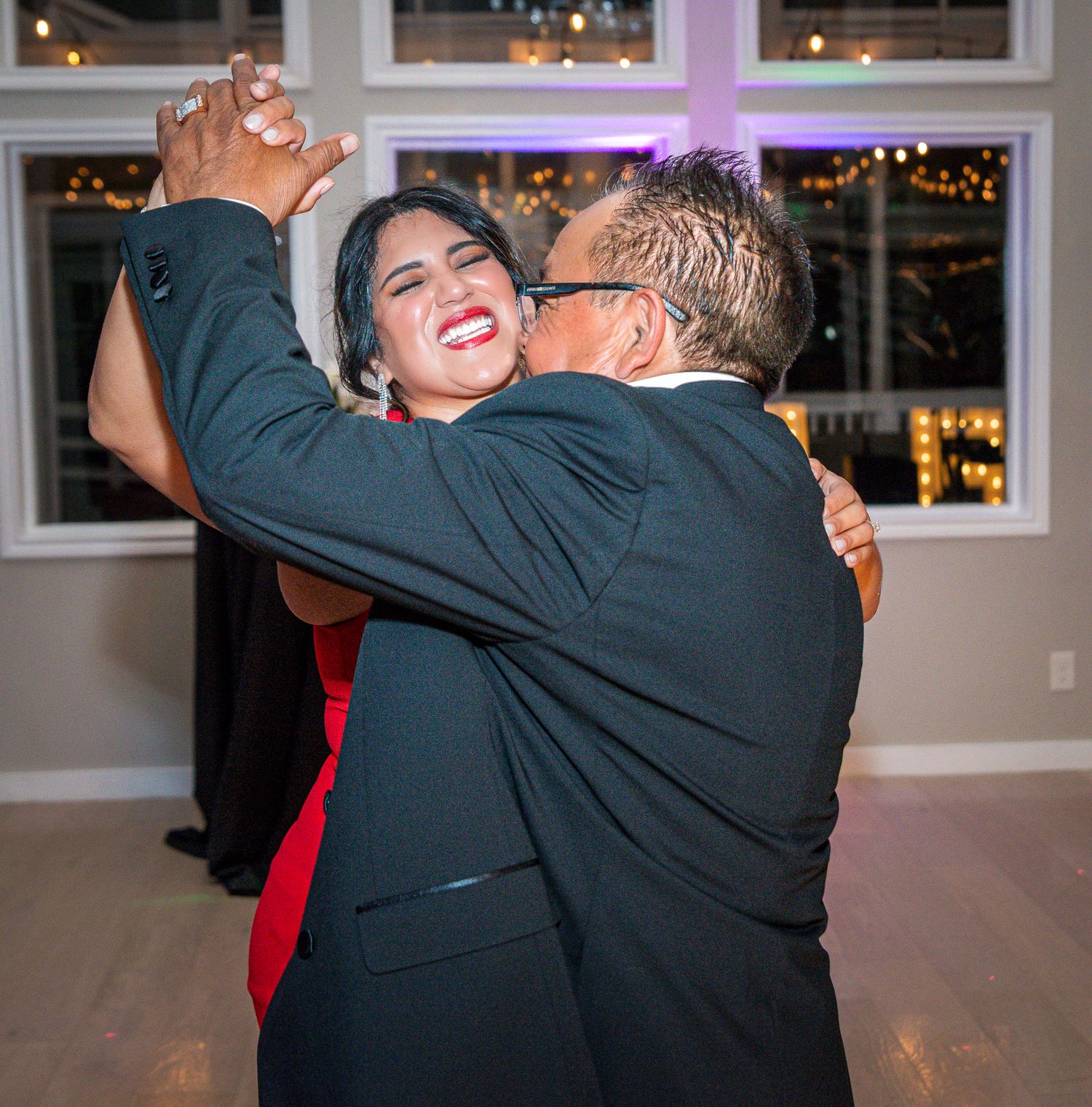 Guests embracing and dancing at an elegant reception with window lighting.