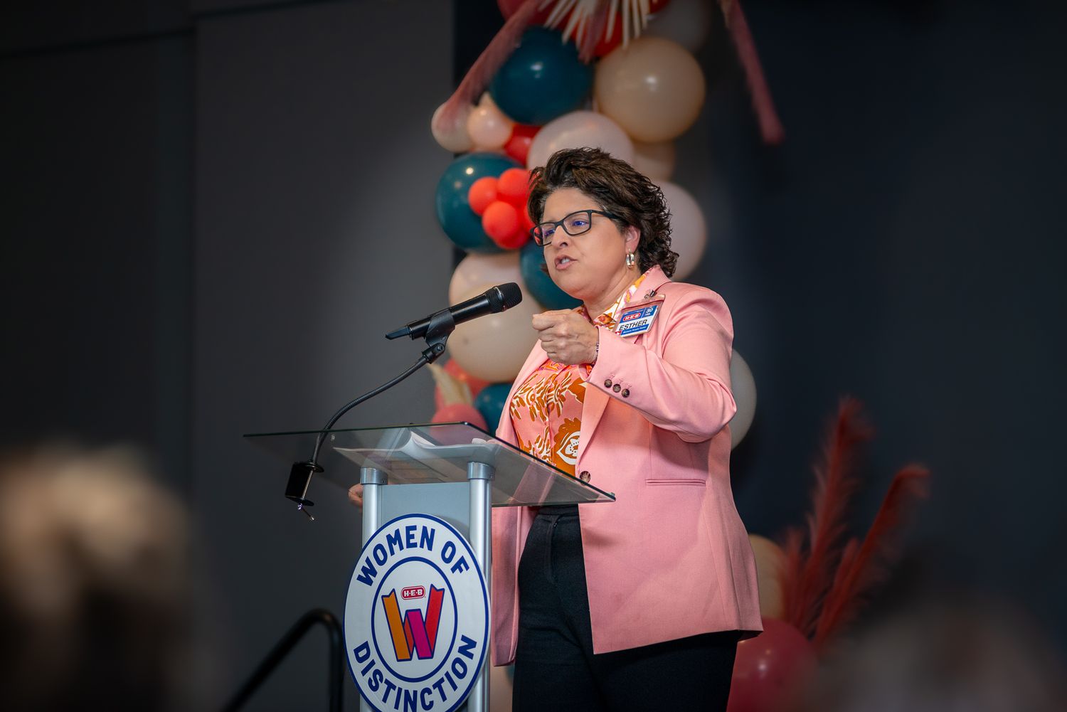 Presenter delivering speech at branded podium with festive balloon decorations.
