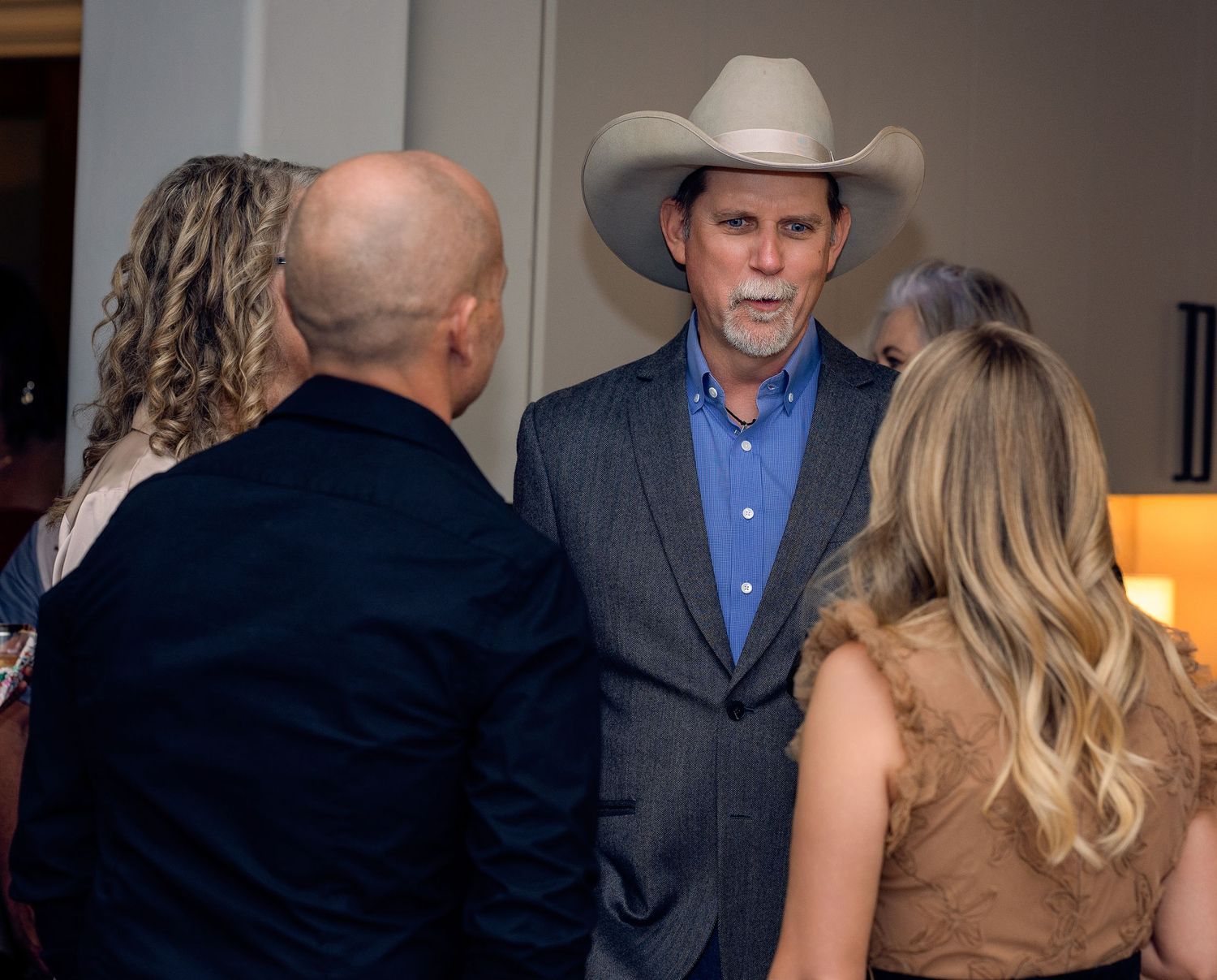 People mingling at a formal indoor event with western attire and cowboy hats.