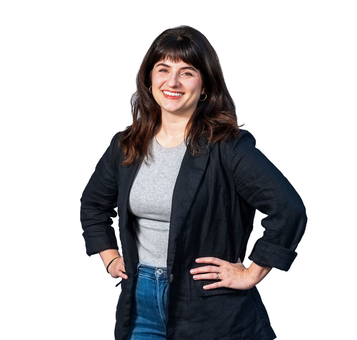 Professional woman in business attire smiling and posing with hands on hips against white background.