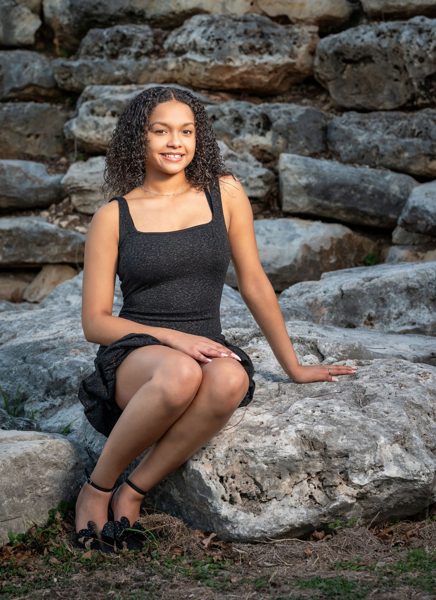A person in a black dress sits on rocky terrain during an outdoor portrait session at sunset.