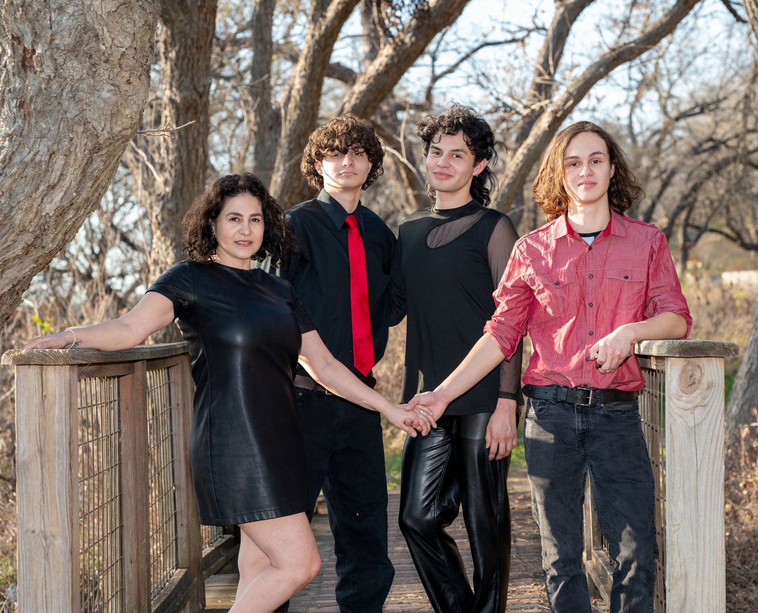 A group poses casually against a wooden fence in an outdoor setting with bare winter trees in the background.