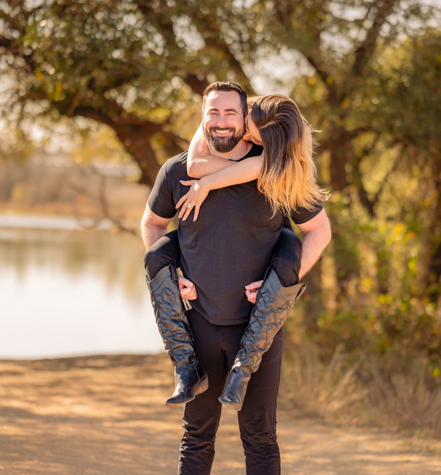 A couple shares a tender embrace outdoors near a lake during golden hour with trees in the background.