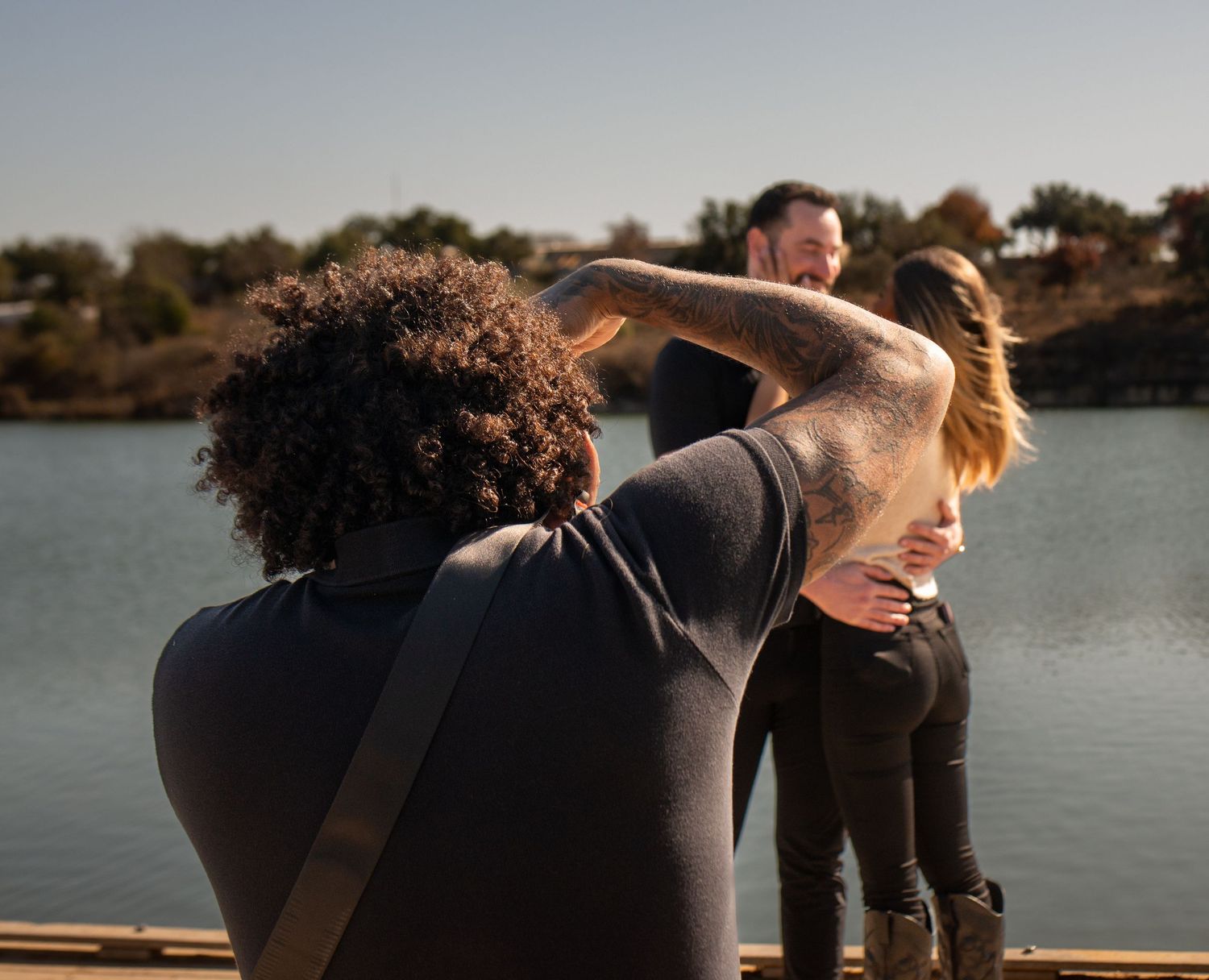 A group of people in black outfits stand on a wooden dock overlooking a serene lake at sunset.