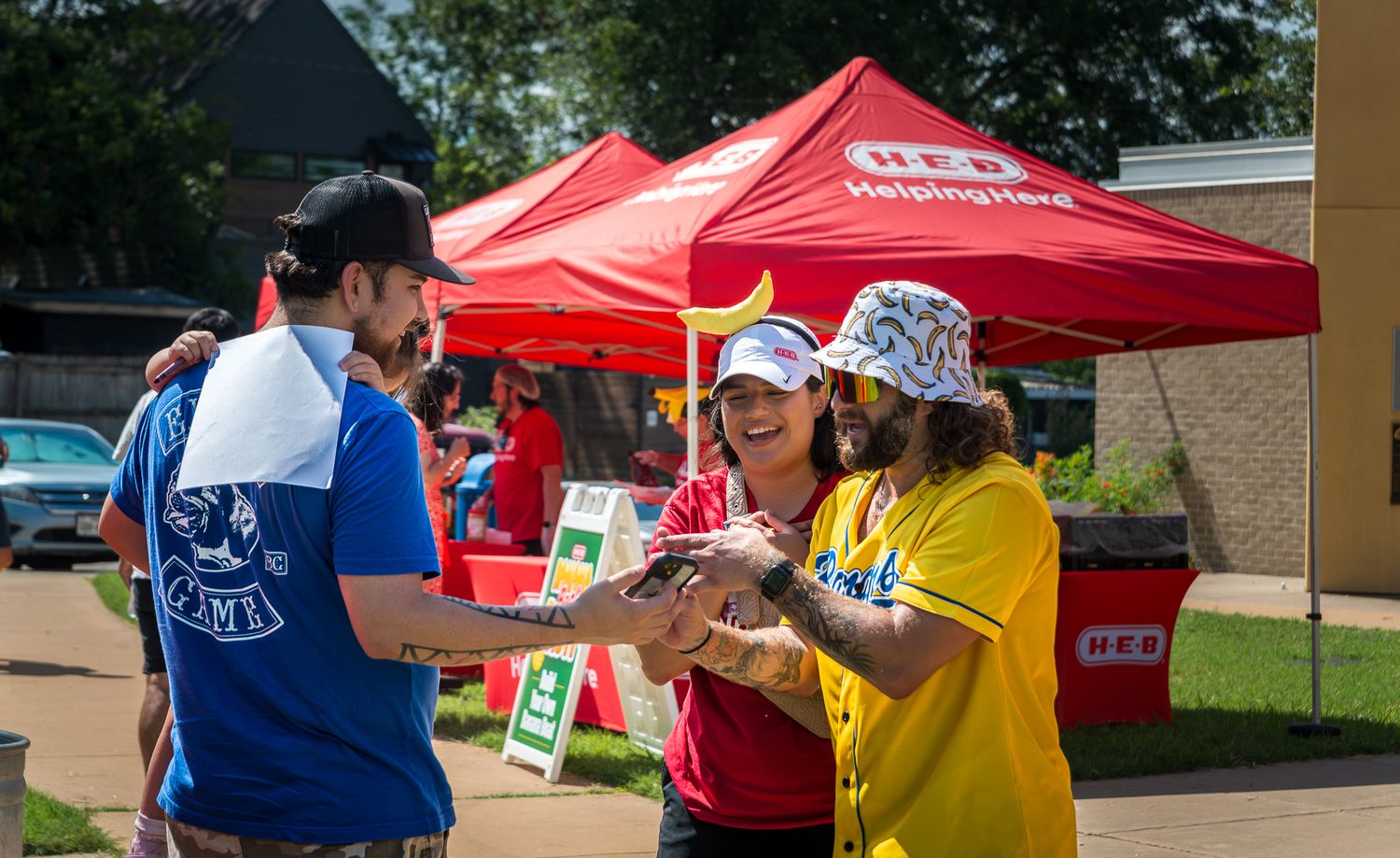 People mingling under red canopy tents at an outdoor community gathering.